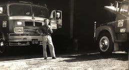 Foto antiga em preto e branco de um caminhão da Covre com o motorista ao lado