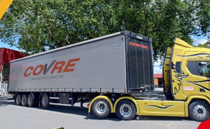 A mesma Scania amarela engatada numa carreta de lona cinza com o COVRE em vermelho