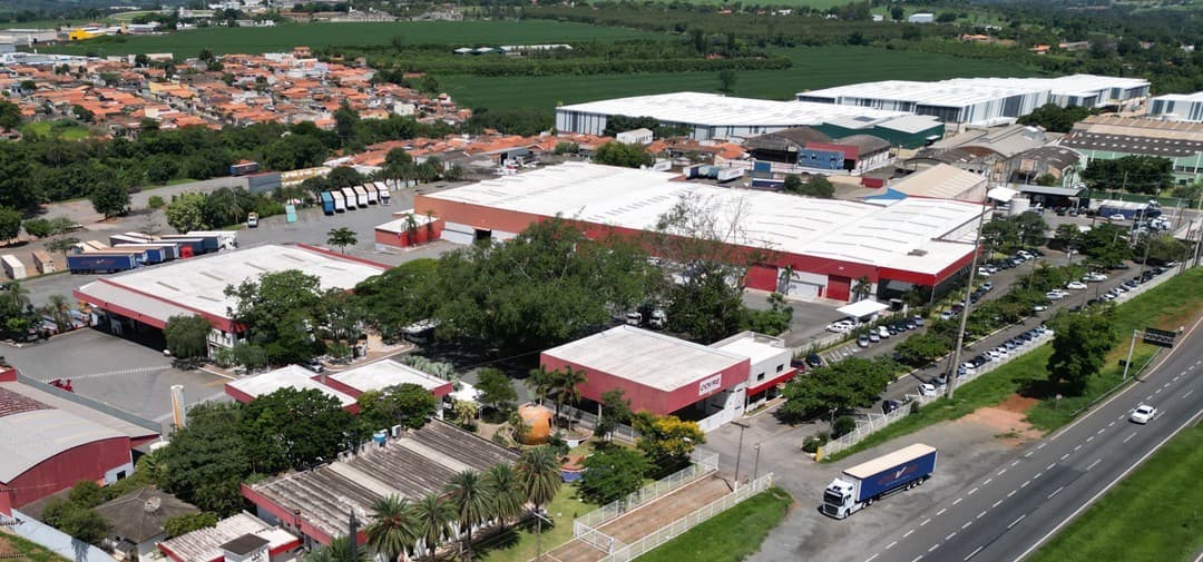 Galpões vermelhos e brancos da Covre e o pátio de carretas, vistos do alto, ao lado da rodovia