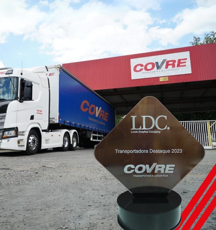 Troféu Transportadora Destaque 2023 da LDC diante de uma carreta Covre e da portaria da matriz